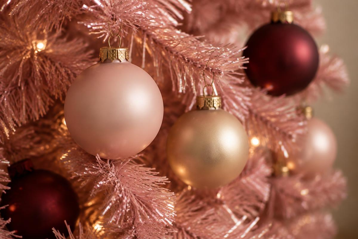 Close view of a pink tinsel tree branch with matte blush, champagne gold and deep burgundy ornaments and warm fairy lights